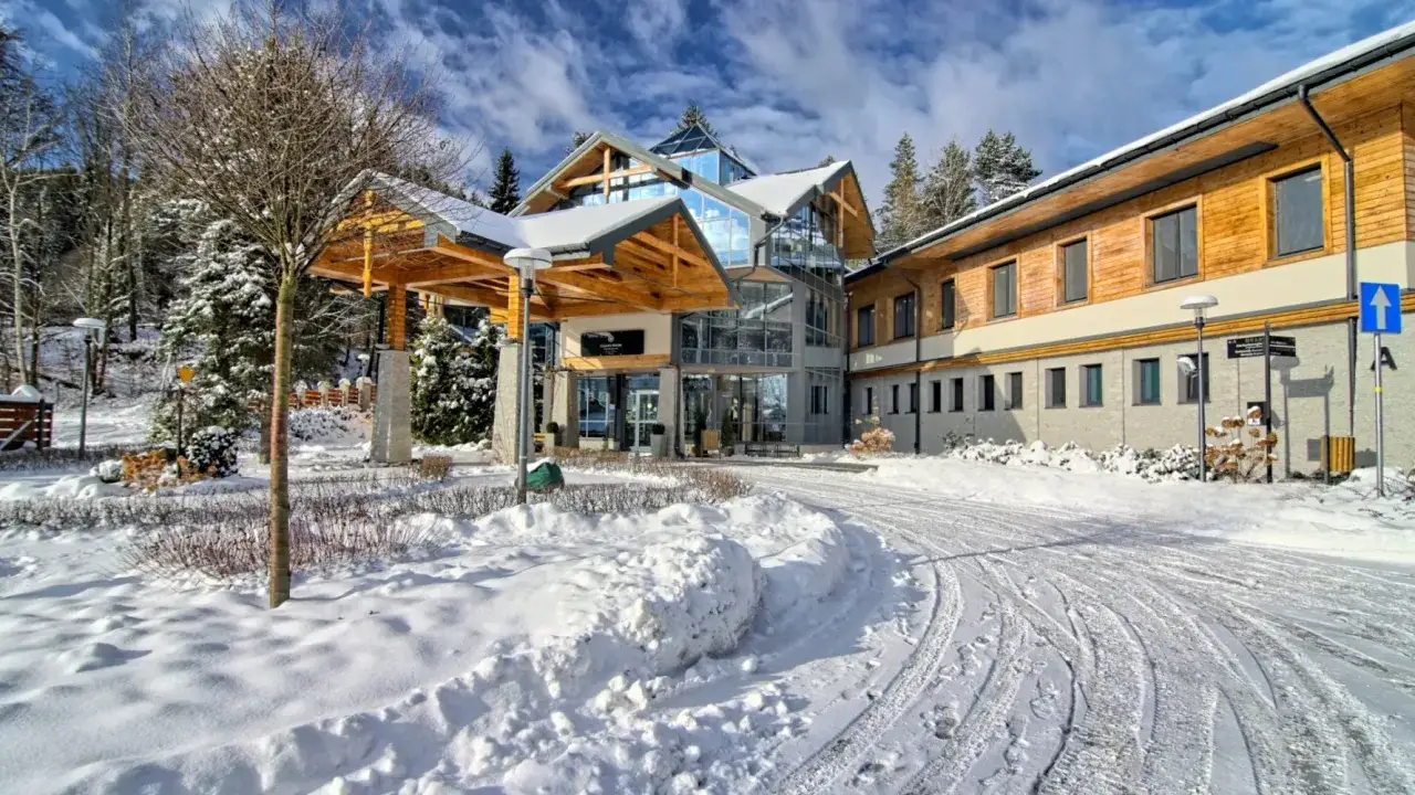 Zimowe święta w g&oacute;rach: nowoczesny hotel otoczony śniegiem i lasem, z drewnianymi elementami i przeszklonym wejściem.