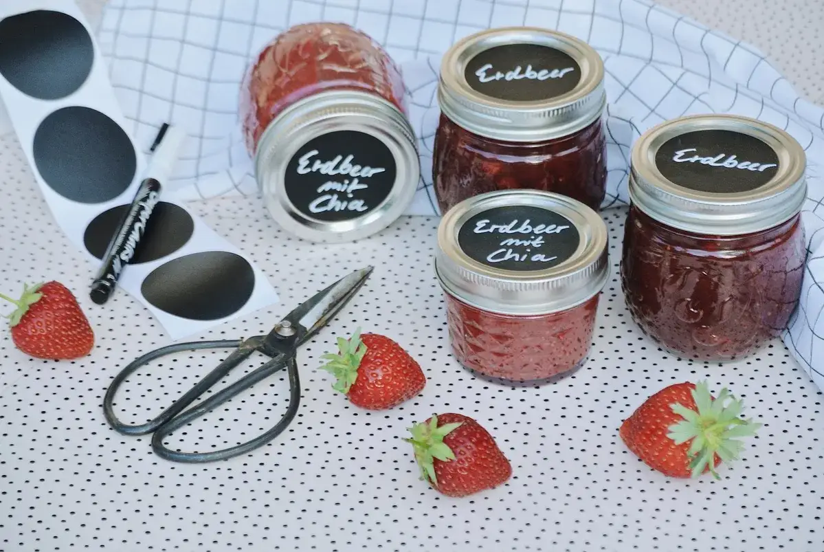 Erdbeermarmelade mit Chia haltbar machen: Gläser, Erdbeeren, Schere und Etiketten liegen bereit.