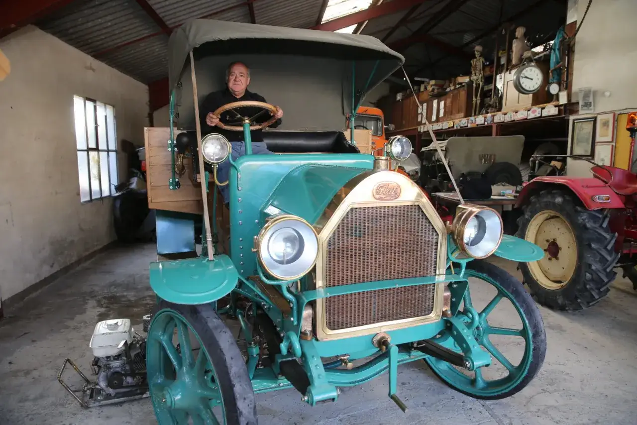 Un homme au volant d'un camion vert &eacute;meraude, un mod&egrave;le des ann&eacute;es 50, dans un garage rempli d'objets anciens.