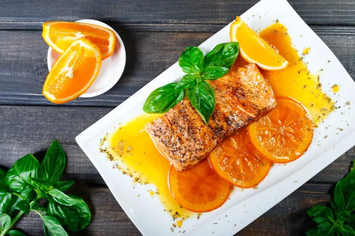 Delicioso salm&oacute;n a la naranja, servido con rodajas de naranja y hojas de albahaca fresca.