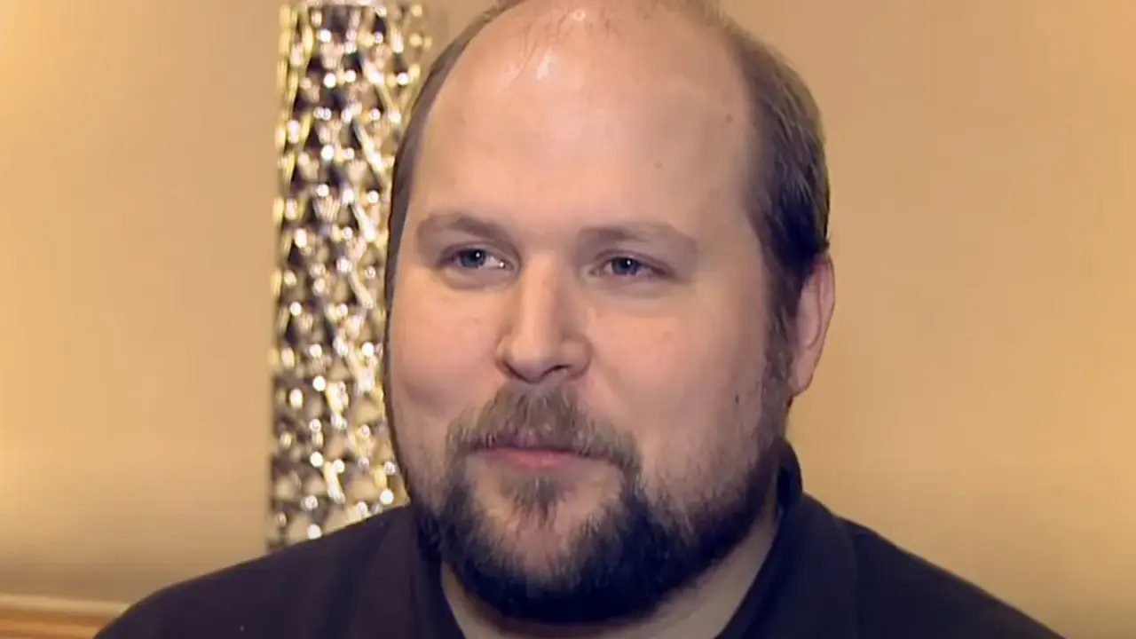 Markus Persson, twórca Minecraft, z charakterystyczną brodą i łysiną, w tle ozdobna lampa.