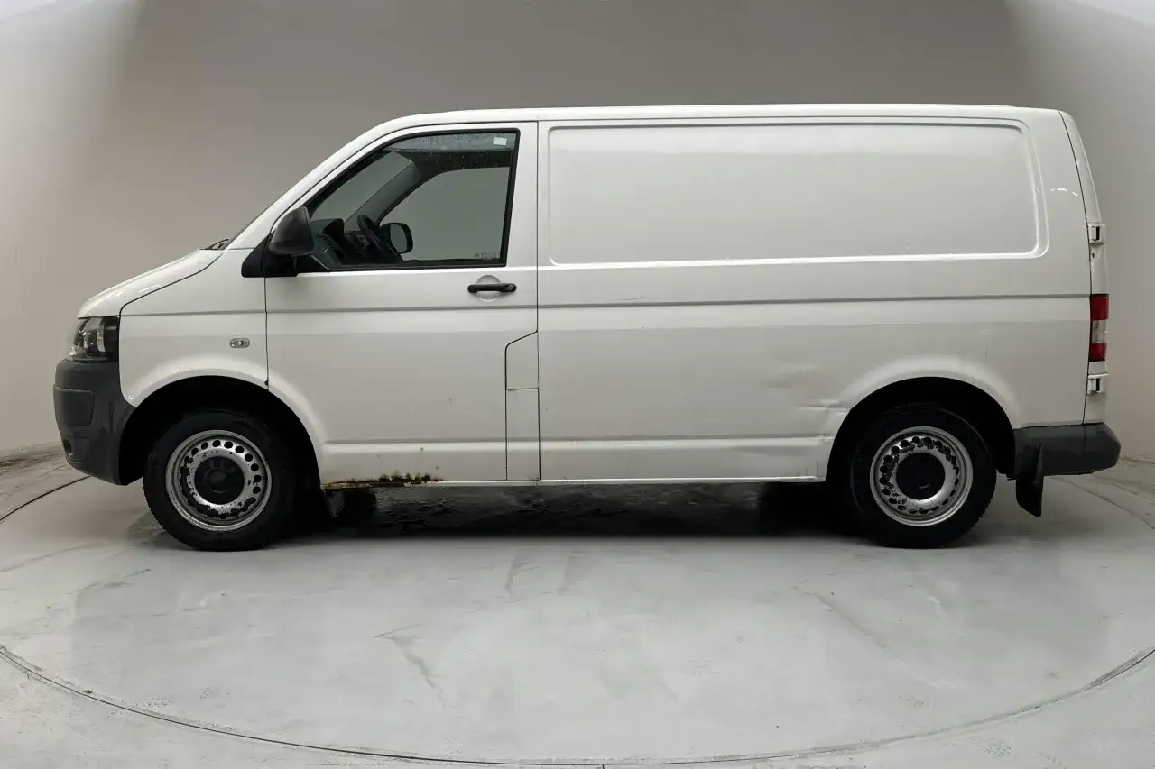 Vit VW Transporter T5 med rostskador längs tröskeln och en buckla på sidan. Ett typiskt vw transporter t5 problem.