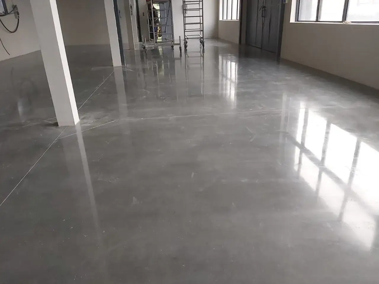 Gładka, polerowana posadzka betonowa, idealna do nowoczesnych wnętrz. Widać odbicia światła i linie dylatacji. Jaki beton na posadzkę? Ten wygląda świetnie!