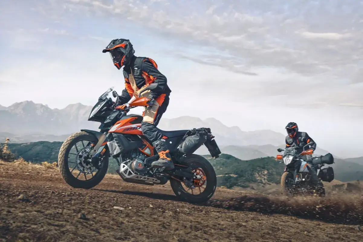 Dos pilotos en sus KTM 490 Adventure conquistan un camino de tierra con montañas al fondo.