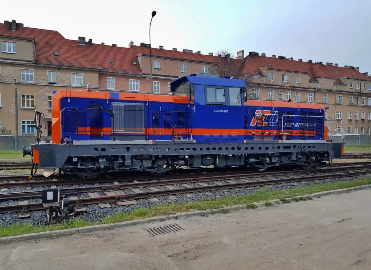 Nowa lokomotywa SM42 w barwach PKP Intercity stoi na torach przed kamienicami.