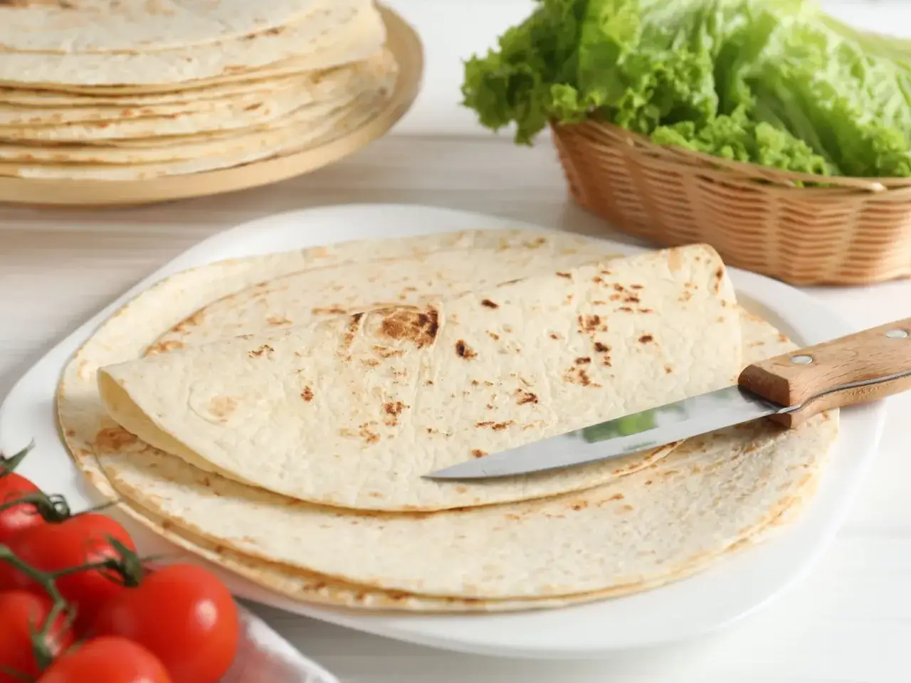 Placki tortilla oryginalny przepis na talerzu, obok pomidorki i sałata. Idealne do wrapów.