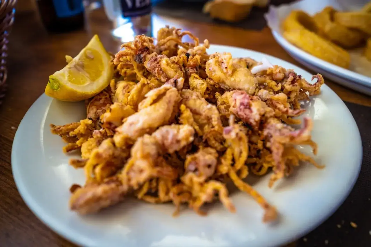 Plato de puntillas de calamar fritas, crujientes y doradas, servido con una rodaja de limón.