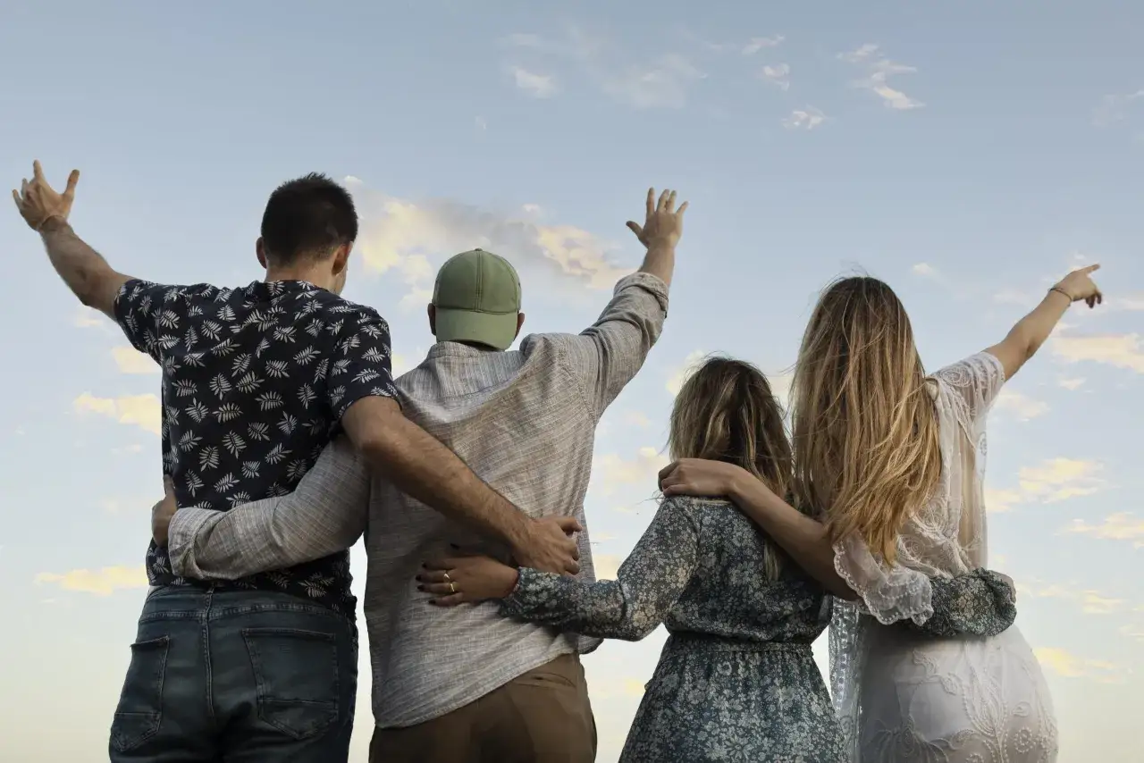 Cuatro amigos celebran la vida y sus relaciones de amistad sanas, con los brazos en alto contra un cielo nublado.