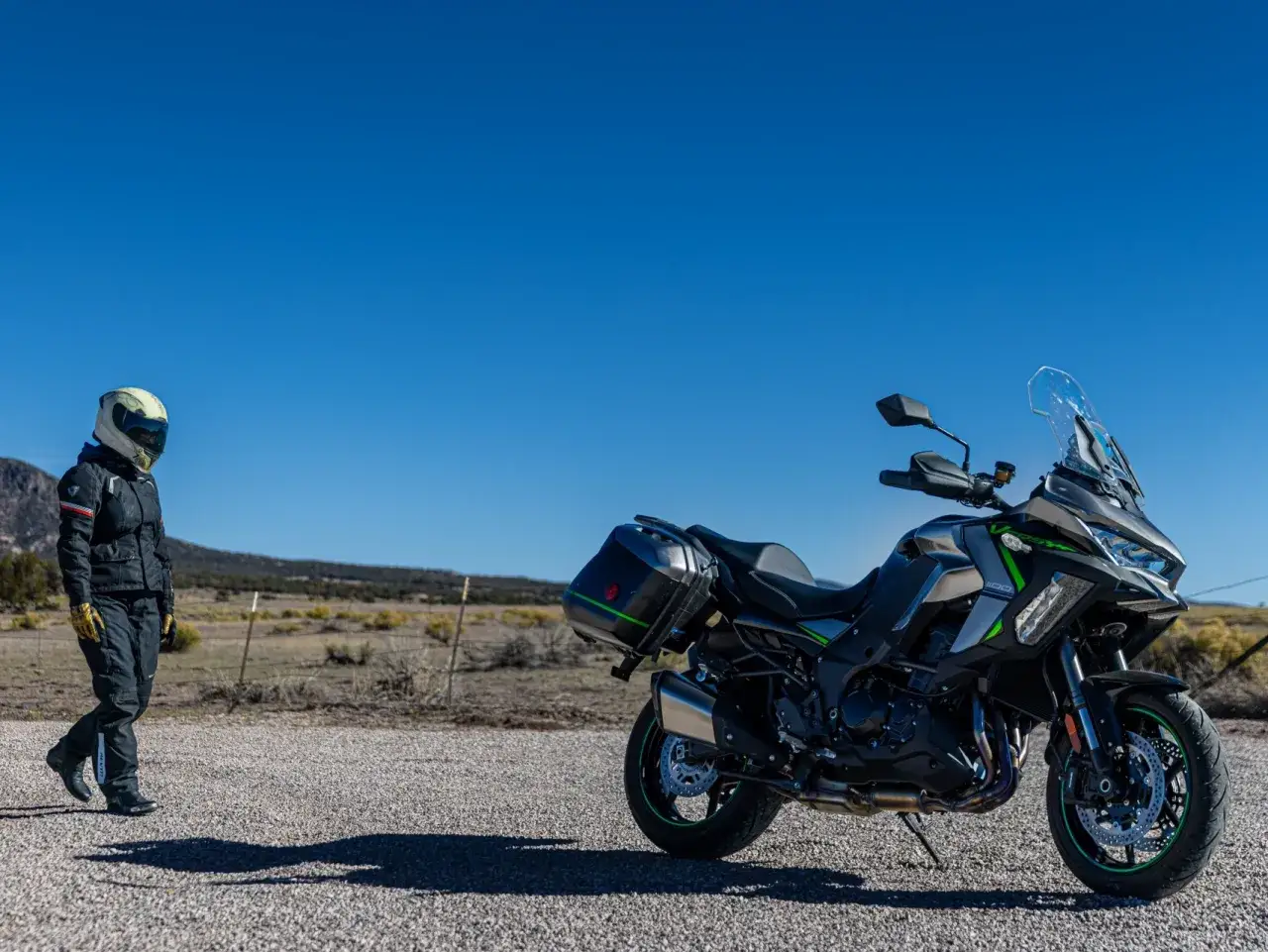Motociclista se acerca a una moto sport turismo lista para la aventura en un paisaje des&eacute;rtico bajo un cielo azul.