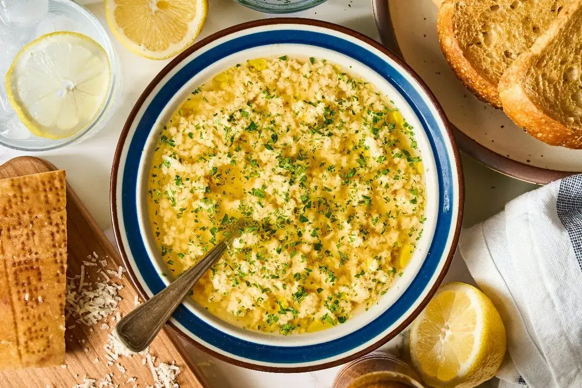 Miseczka zupy stracciatella, ozdobiona natką pietruszki, obok cytryny, grzanek i kawałka parmezanu.