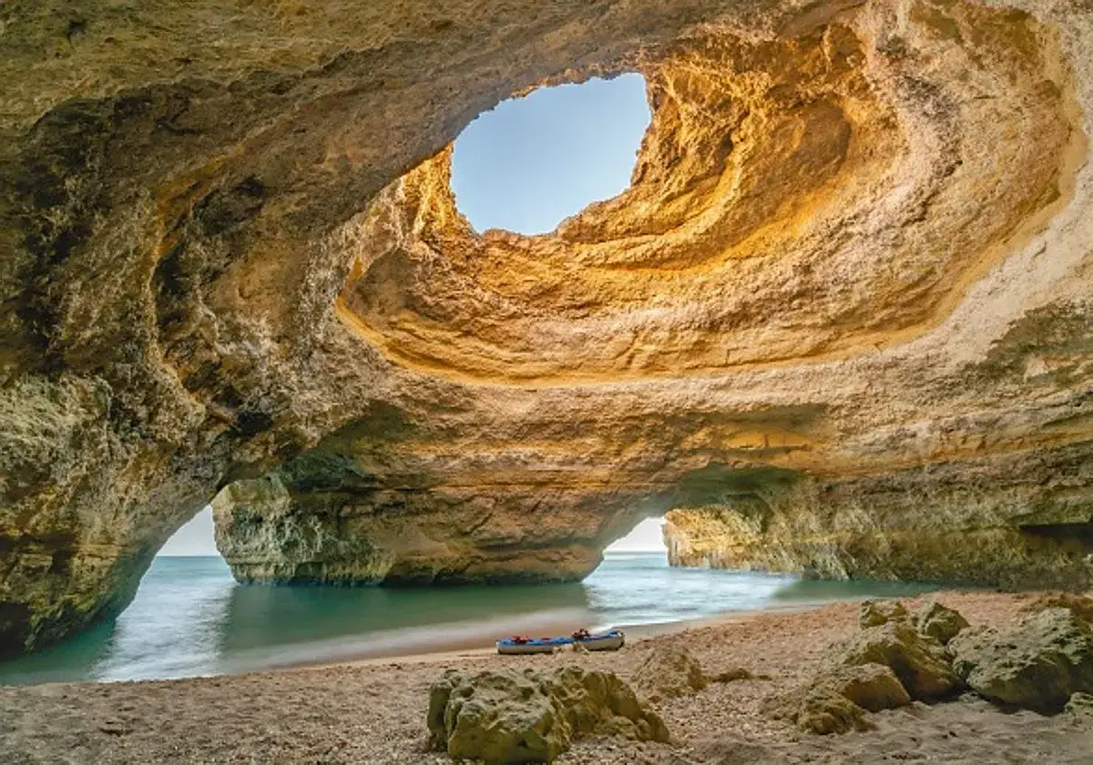 Dos kayaks esperan en la arena de una cueva marina en el Algarve, perfectos para explorar las **actividades Algarve** y sus costas.