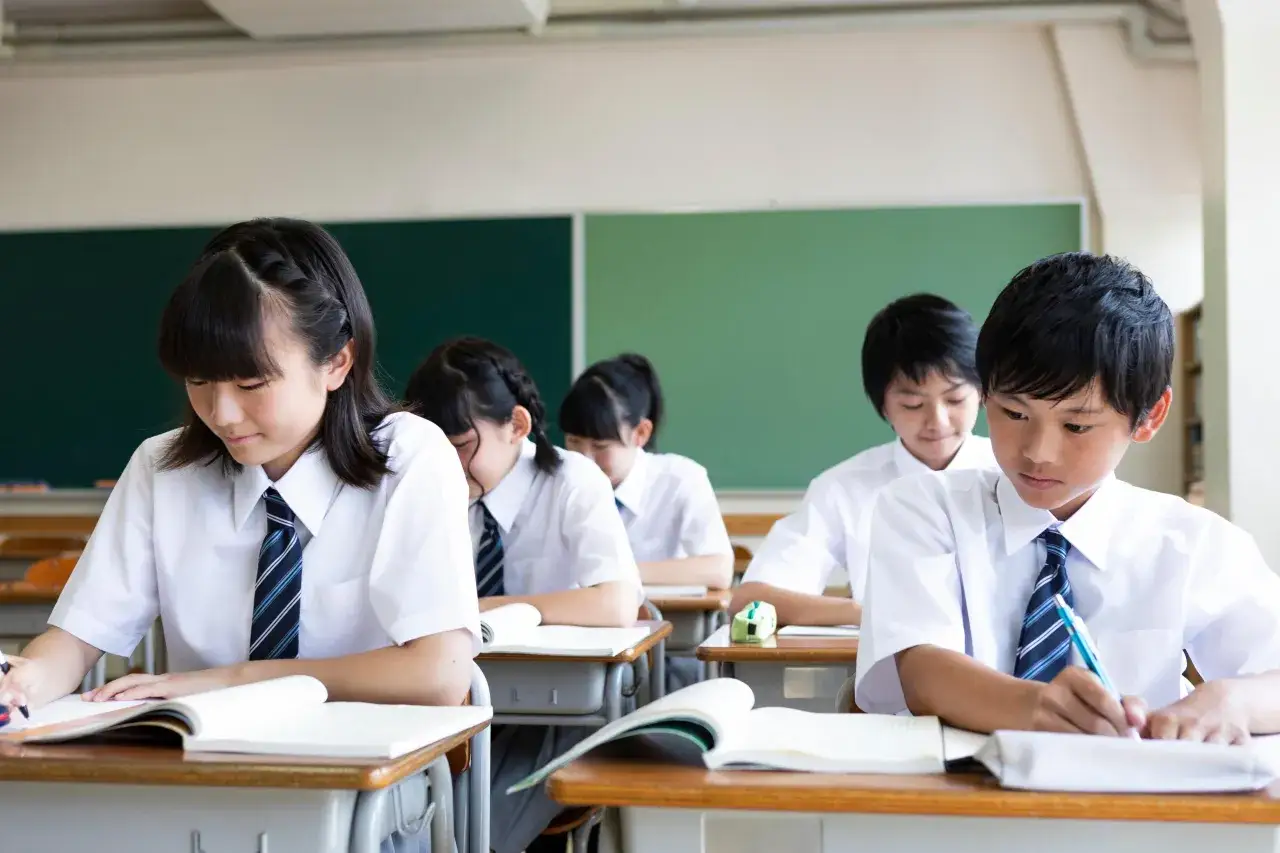 Uczniowie w szkolnych mundurkach siedzą w ławkach. Wszyscy skupieni są na lekcji w szkole w Japonii.
