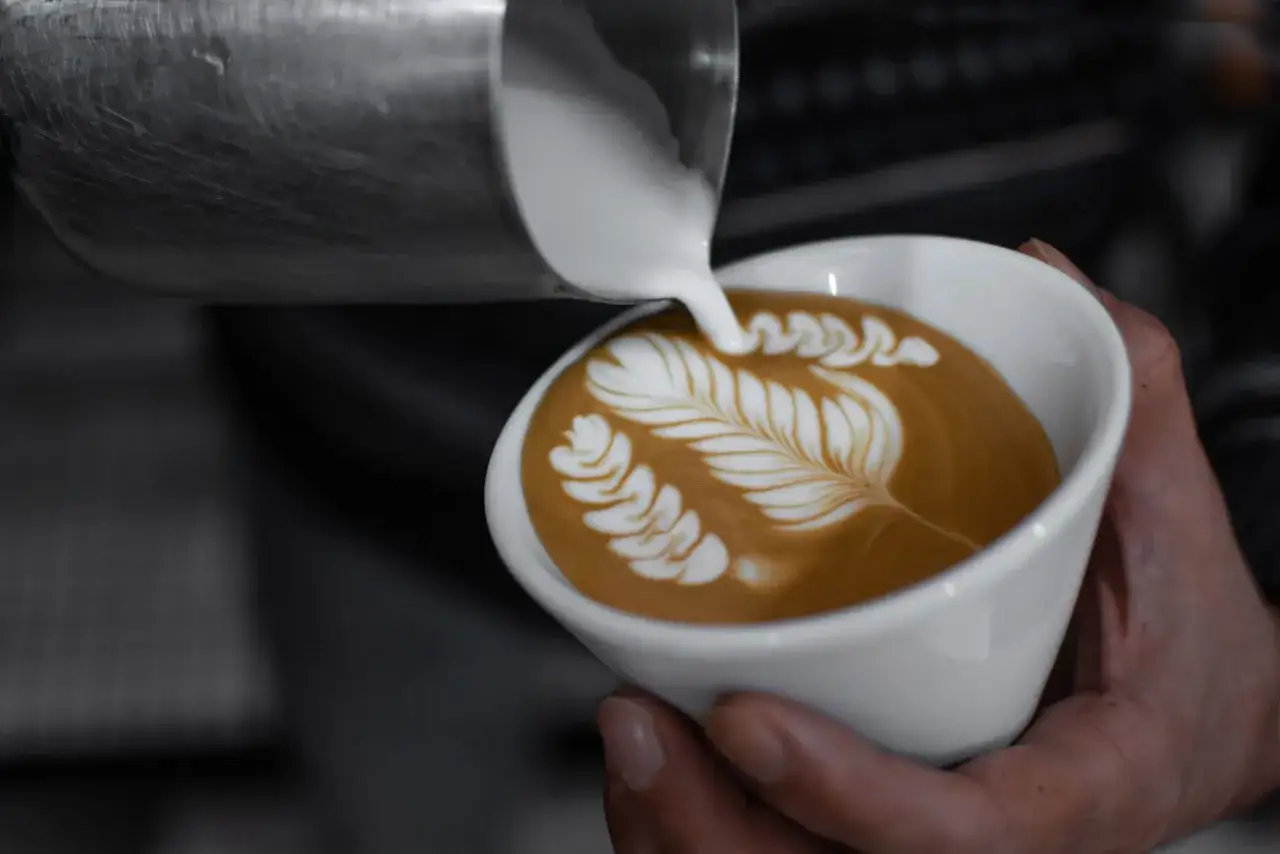 Un barista crea un'arte del caffè con schiuma di latte, un design a foglia su un cappuccino.