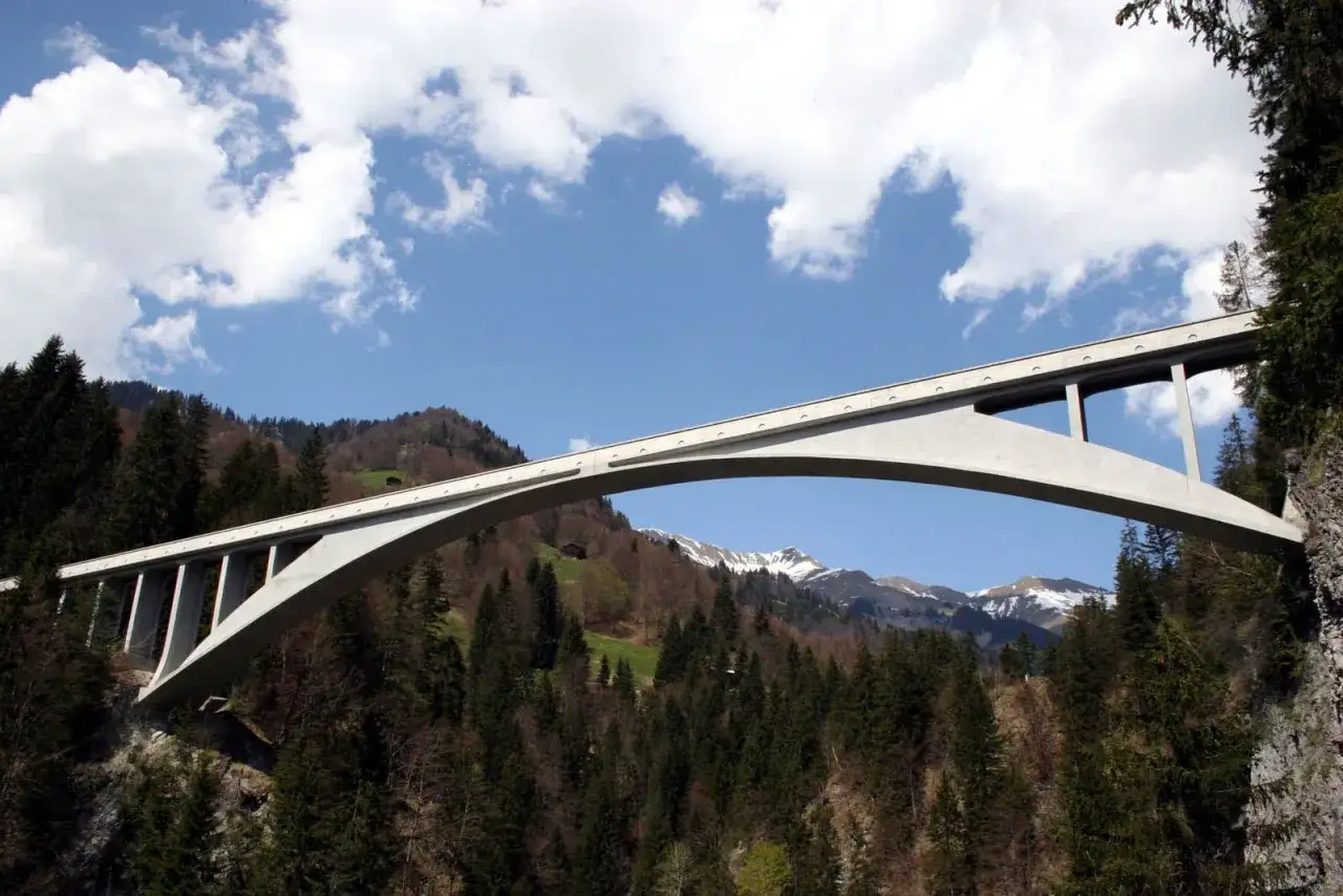 El puente de Salginatobel se alza majestuoso sobre un valle boscoso, con picos nevados al fondo.