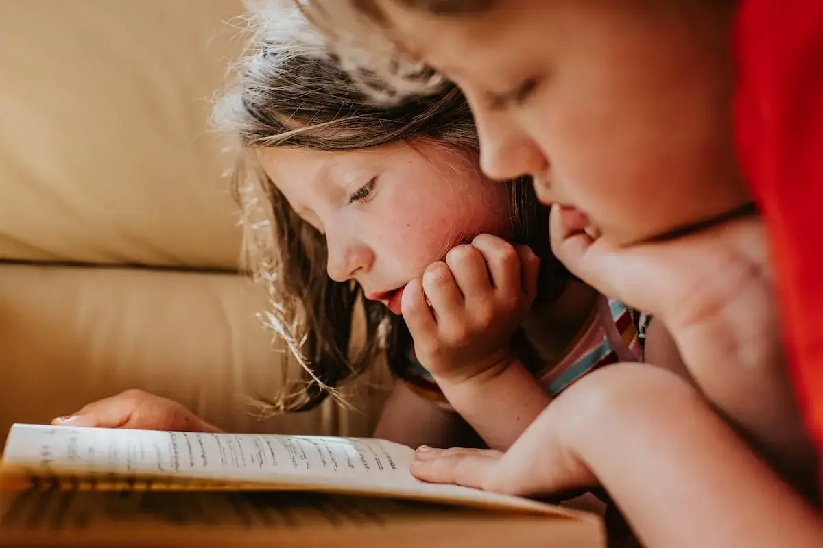 Dos ni&ntilde;os concentrados en un libro. La pregunta de a qu&eacute; edad se aprende a leer se responde con esta imagen de aprendizaje.