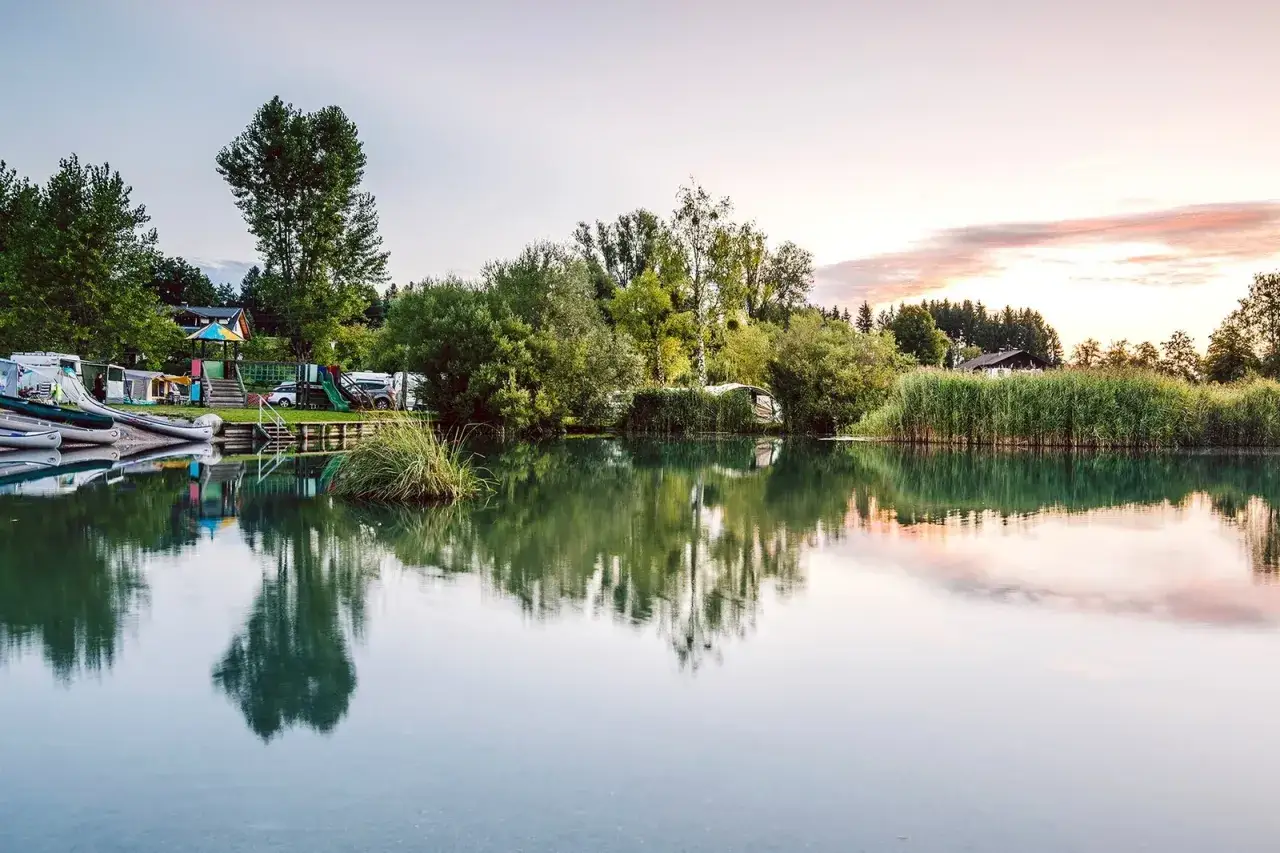 Spokojny poranek nad jeziorem w Karyntii, Austria. Kemping z łodziami i przyczepami kempingowymi, otoczony zielenią i trzcinami.