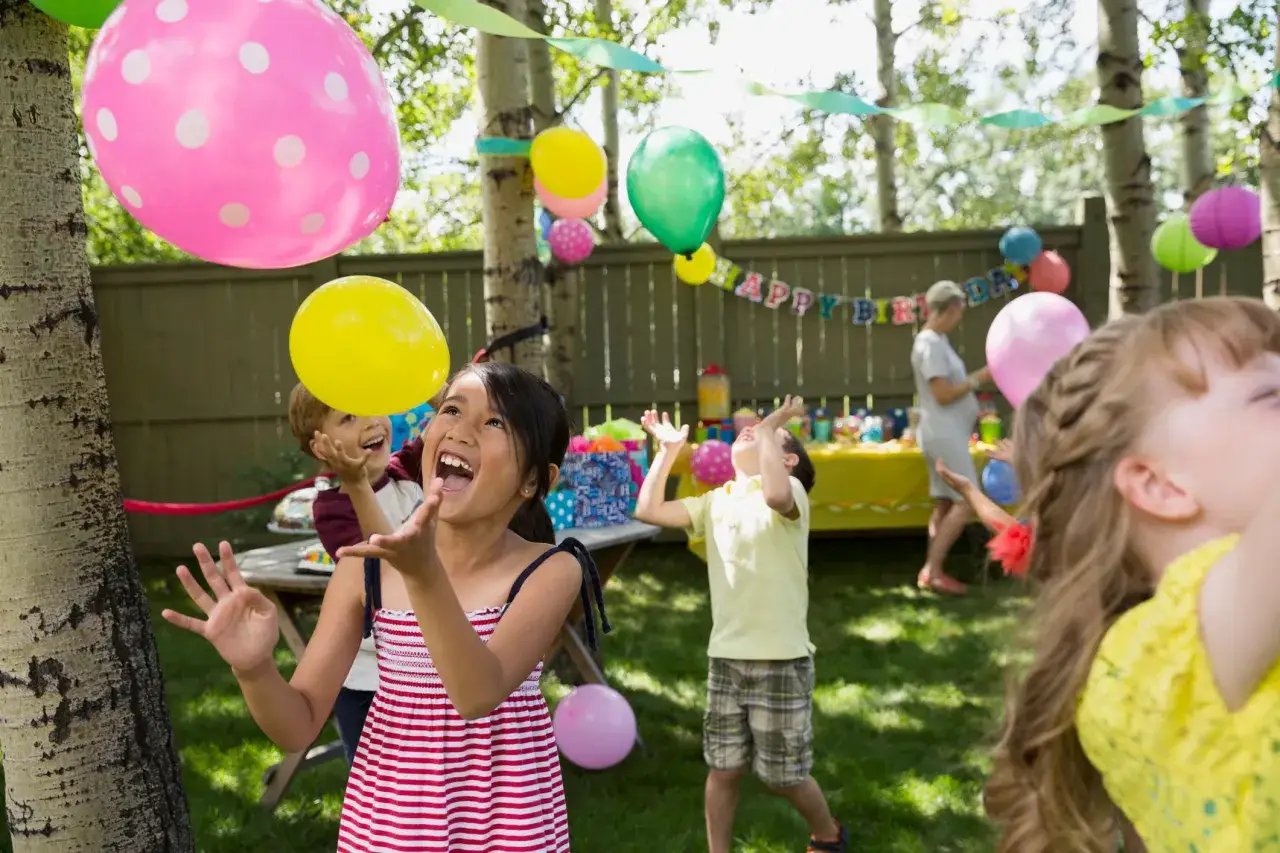 Barn njuter av kalaslekar 5 &aring;r med ballonger i tr&auml;dg&aring;rden. Glada barn hoppar och f&aring;ngar f&auml;rgglada ballonger.