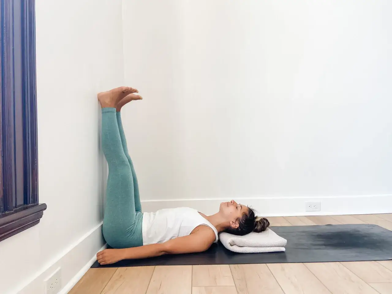 Mujer en postura de yoga con piernas elevadas contra la pared. Considera las posturas invertidas yoga contraindicaciones para tu práctica.