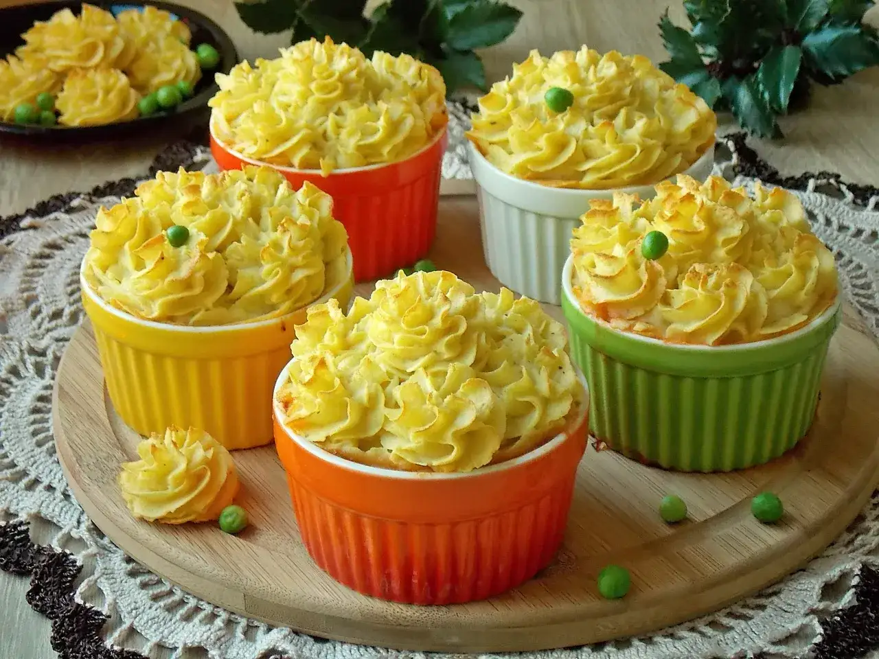 Pięć kolorowych kokilek z ziemniaczanym puree, ozdobionych groszkiem. Jedna kokilka leży obok.