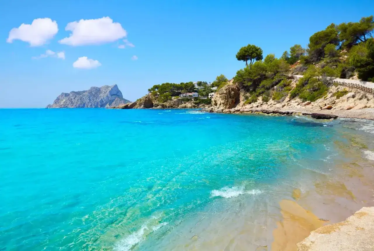 Aguas turquesas y arena dorada en una cala idílica, una de las muchas playas cerca de Calpe, con el Peñón de Ifach al fondo.