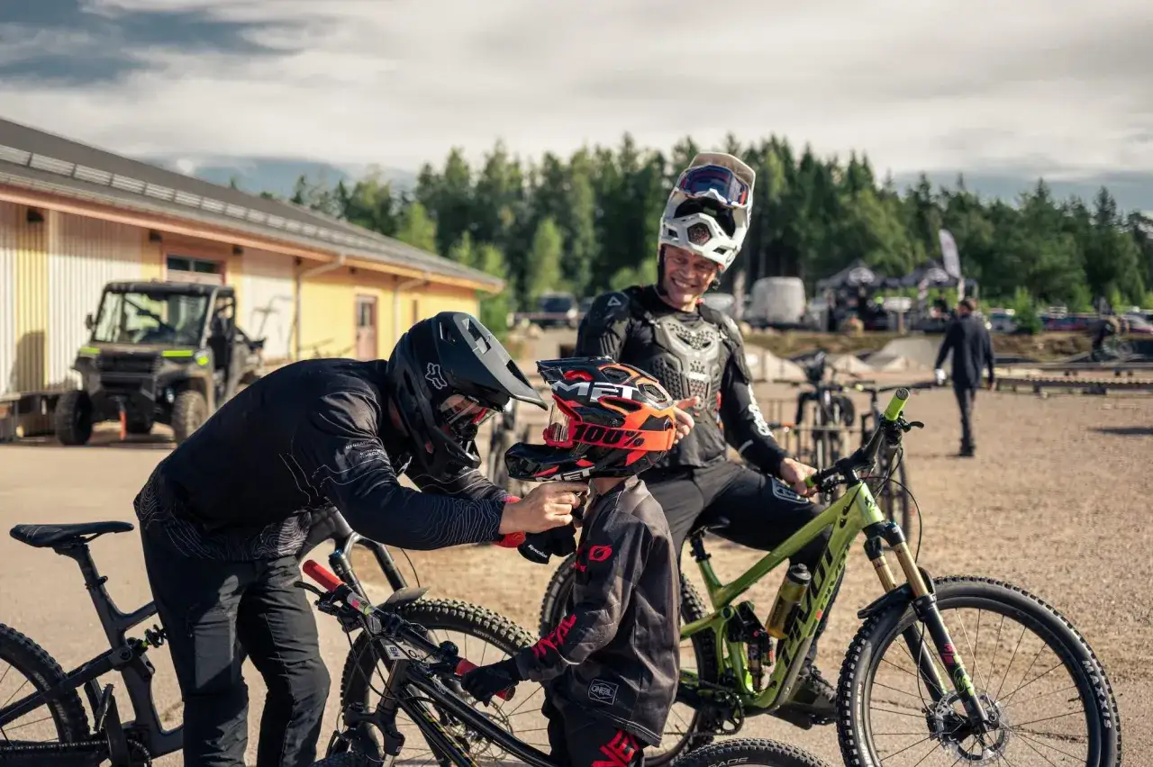 Tv&aring; cyklister f&ouml;rbereder sig f&ouml;r mtb downhill. En vuxen hj&auml;lper ett barn med hj&auml;lmen.
