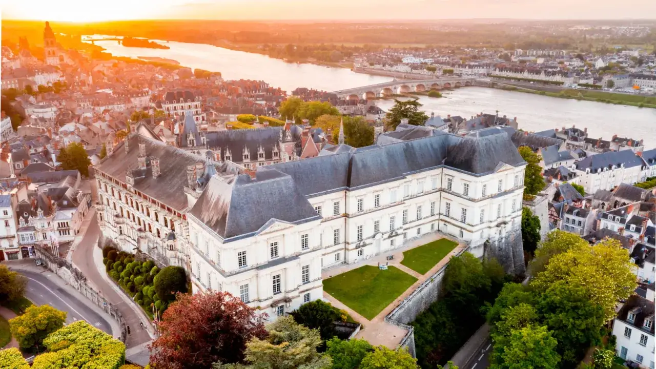 Vue aérienne du château de Blois au coucher du soleil, avec la Loire et la ville en arrière-plan.