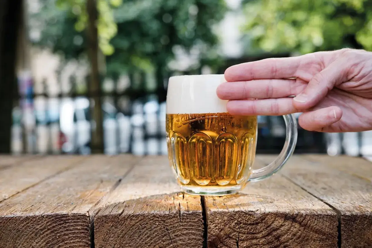 Dłoń trzymająca kufel piwa pilsner. Mętność w piwach typu pilsner haize może wynikać z różnych czynników, np. z białek.