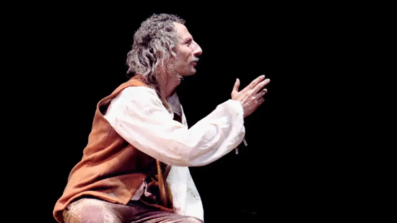 Actor con cabello rizado y barba, vestido como el brujo en el Teatro de las Esquinas, gesticula con las manos.