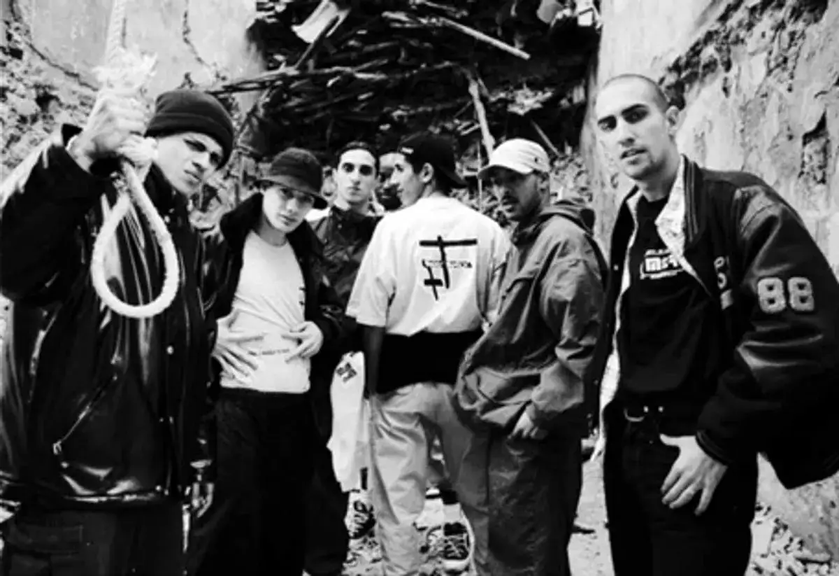 Un groupe de jeunes hommes, symboles de l'histoire du rap français, posent devant un mur délabré. L'un tient une corde, l'autre un logo distinctif.