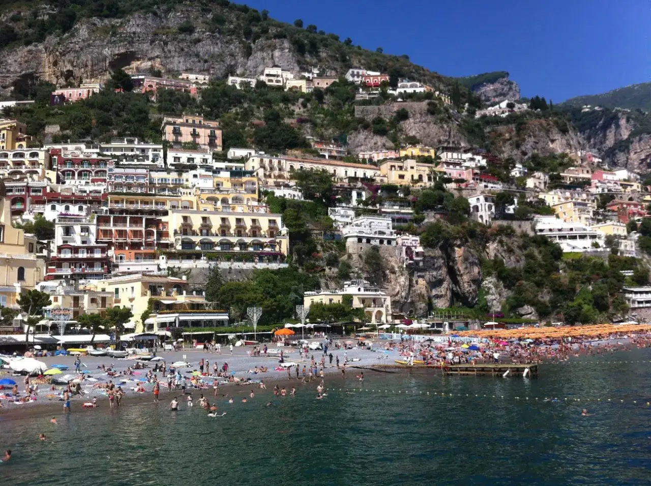 Case colorate aggrappate alla roccia, una spiaggia affollata e il mare blu: la meta costiera amalfitana in tutto il suo splendore.