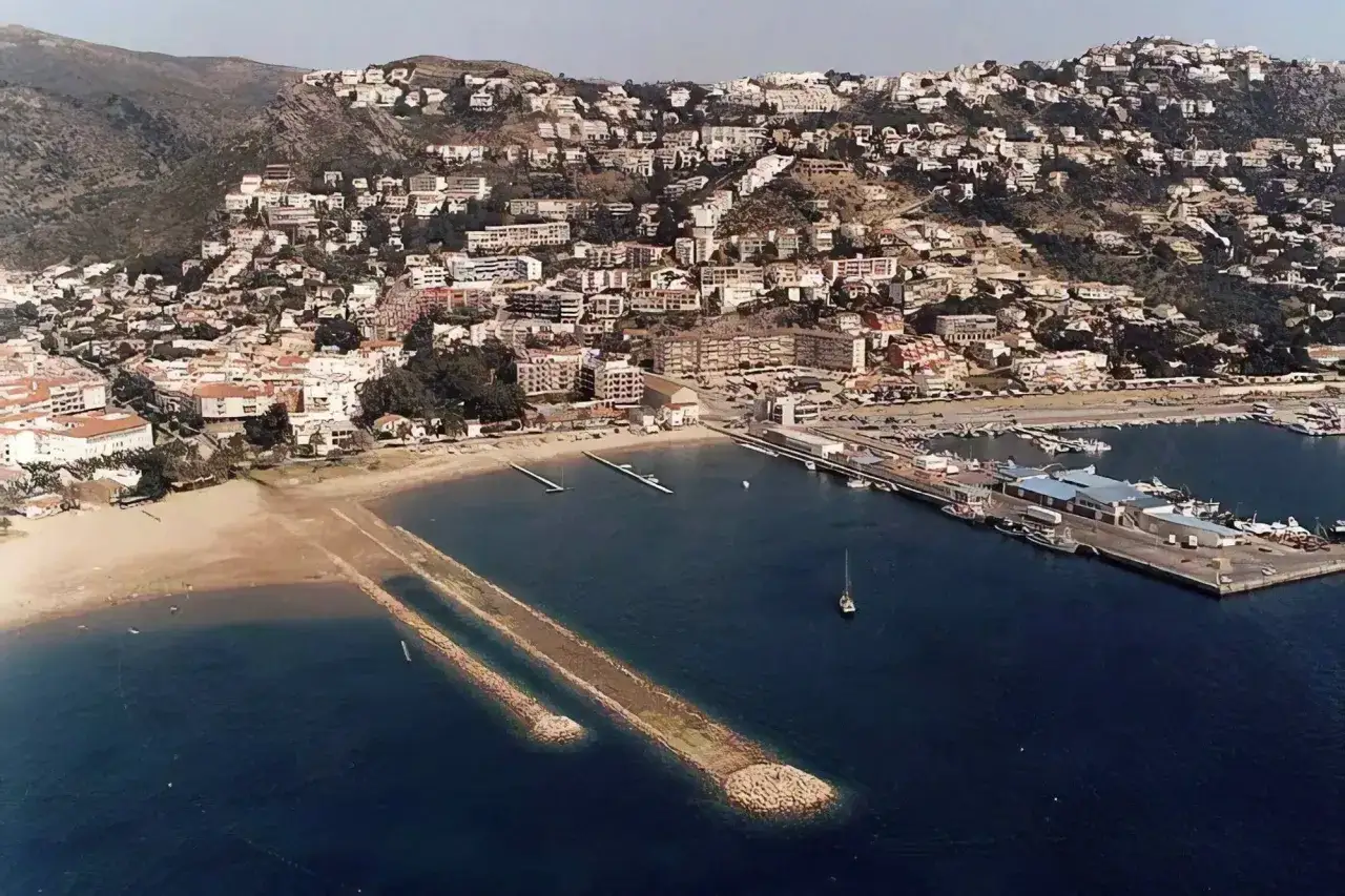 Vista aérea de la playa de la punta, con casas en la ladera y un puerto deportivo lleno de barcos.
