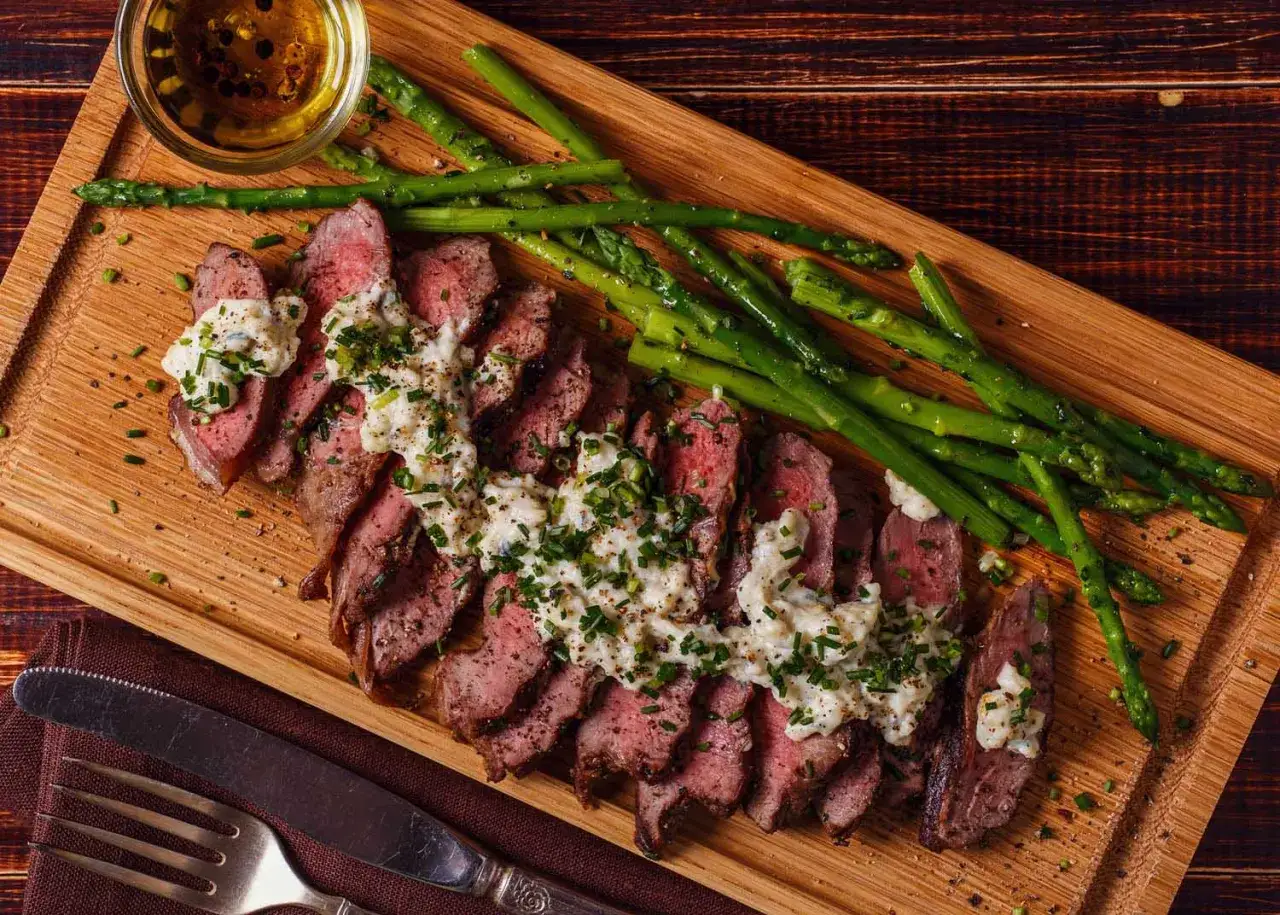 Tranches de steak juteux nappées d'une sauce au bleu crémeuse, accompagnées d'asperges vertes croquantes sur une planche en bois.