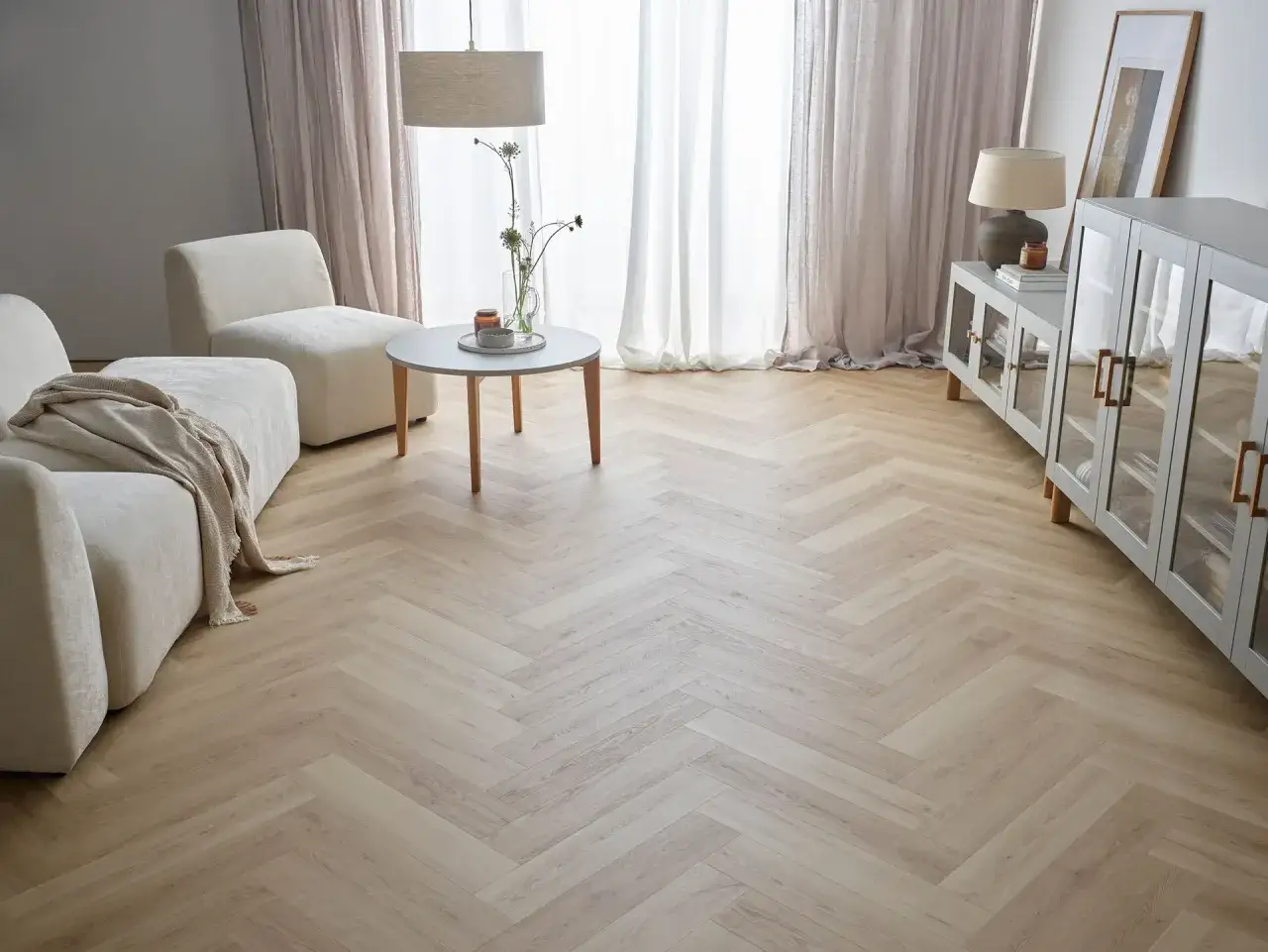 Jasne, oto propozycja:

Eleganckie wnętrze z jasnymi meblami i zasłonami. Centralnym punktem jest podłoga z paneli ułożonych we wzór jodełki, nadająca pomieszczeniu ciepły i stylowy charakter.