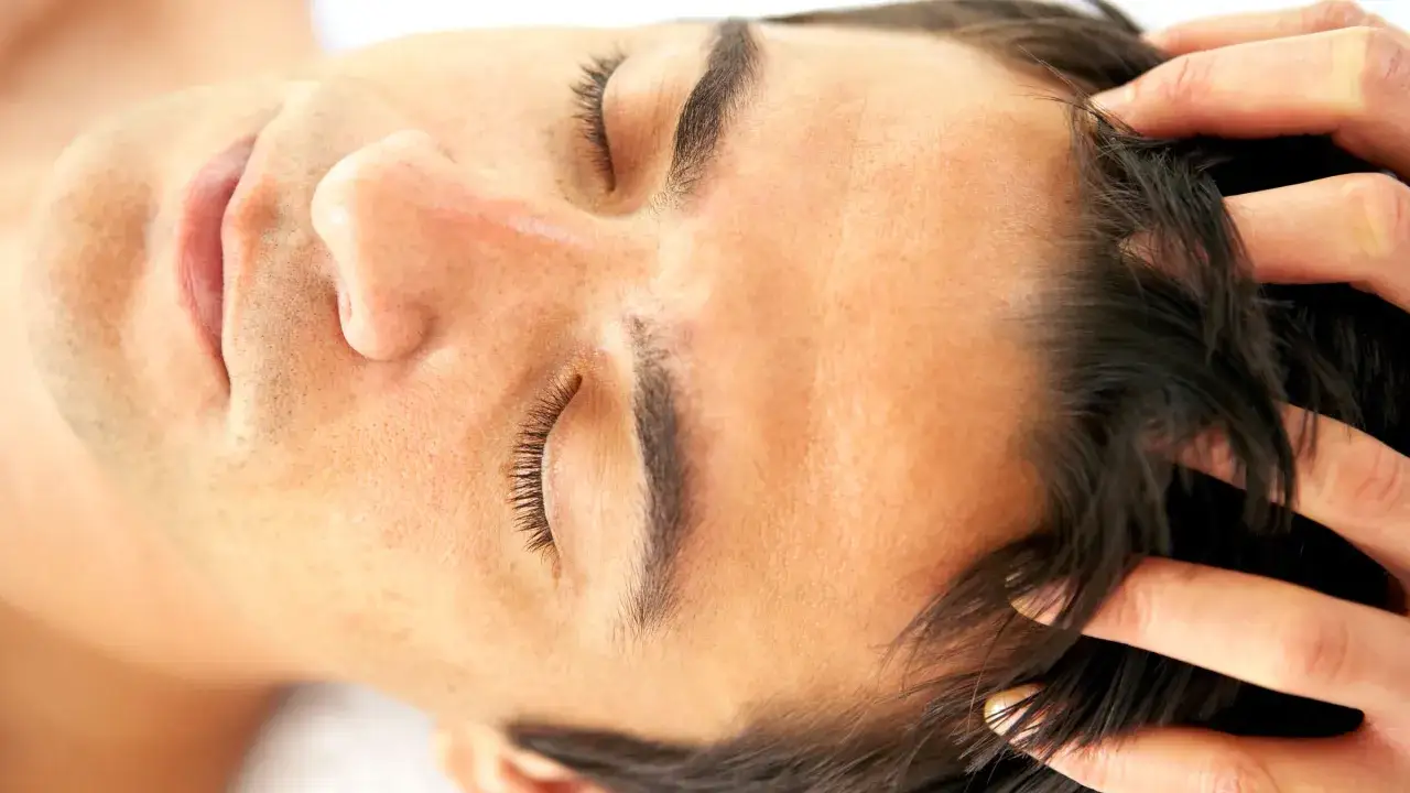 Man con ojos cerrados, recibiendo un masaje capilar para ayudar a recuperar pelo entradas naturalmente.