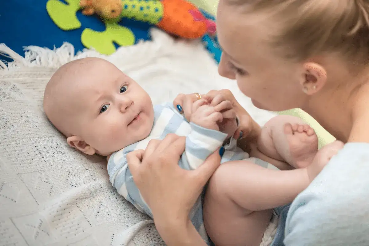 Mama pr&oacute;buje zachęcić 3 miesięczne dziecko, kt&oacute;re nie chce leżeć na brzuchu, do zabawy.