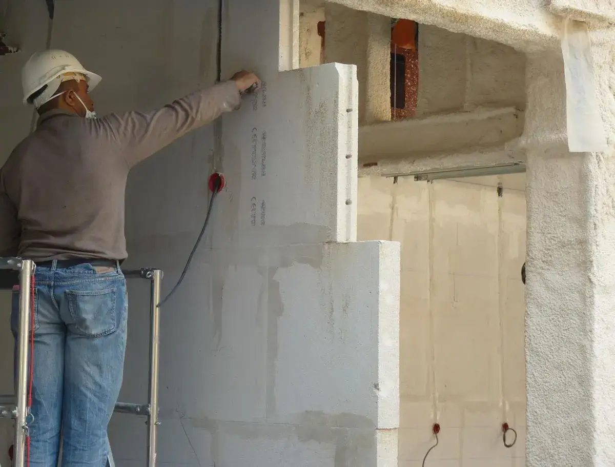 Un ouvrier sur un échafaudage pose des blocs de béton cellulaire pour l'isolation d'un mur.