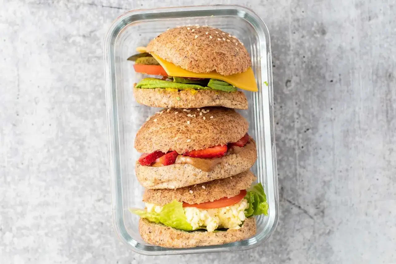 Gestapelte low carb sandwiches in einer Glasbox: Eines mit Avocado, K&auml;se und Gurke, ein anderes mit Erdbeeren und Erdnussbutter, das unterste mit Ei und Salat.