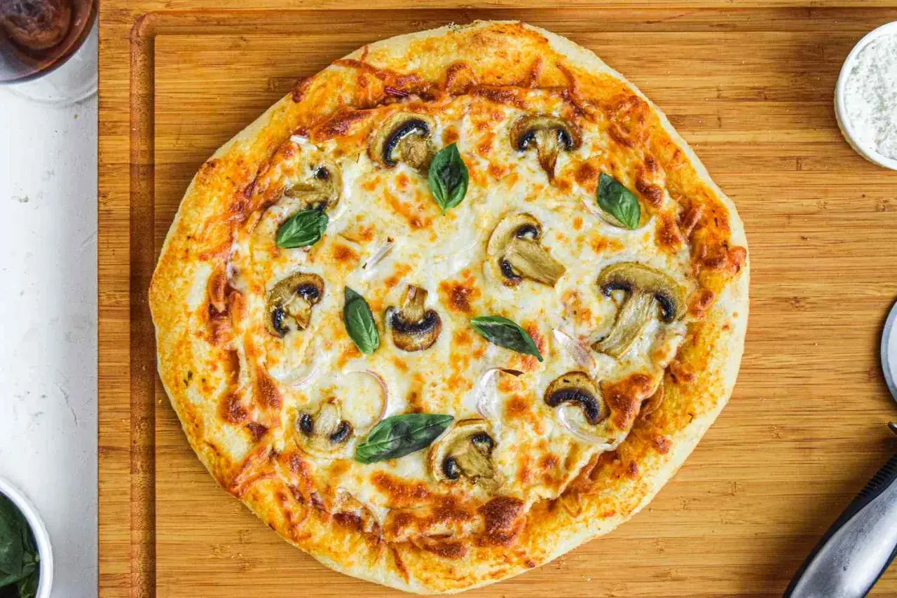 Pyszna pizza z pieczarkami i mozzarellą na cieście bez wyrastania, ozdobiona listkami bazylii.