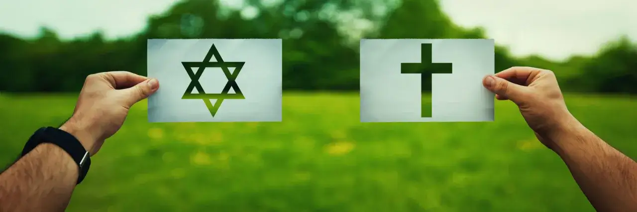 Dwie ręce trzymają kartki z symbolami: Gwiazda Dawida i krzyż. To wizualne przedstawienie judaizmu a chrześcijaństwa.
