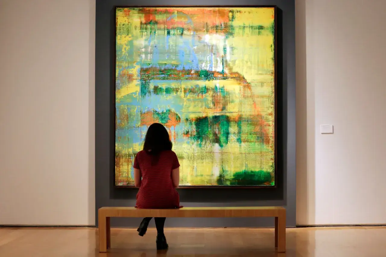 A woman contemplates a vibrant abstract painting, a piece that might fetch a significant sum, reflecting Gerhard Richter's net worth.