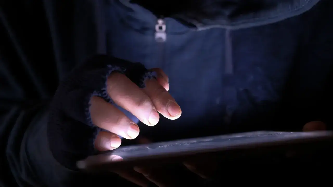 Dłoń w rękawiczce bez palc&oacute;w pisze na tablecie, grożenie postępowaniem karnym wisi w powietrzu.