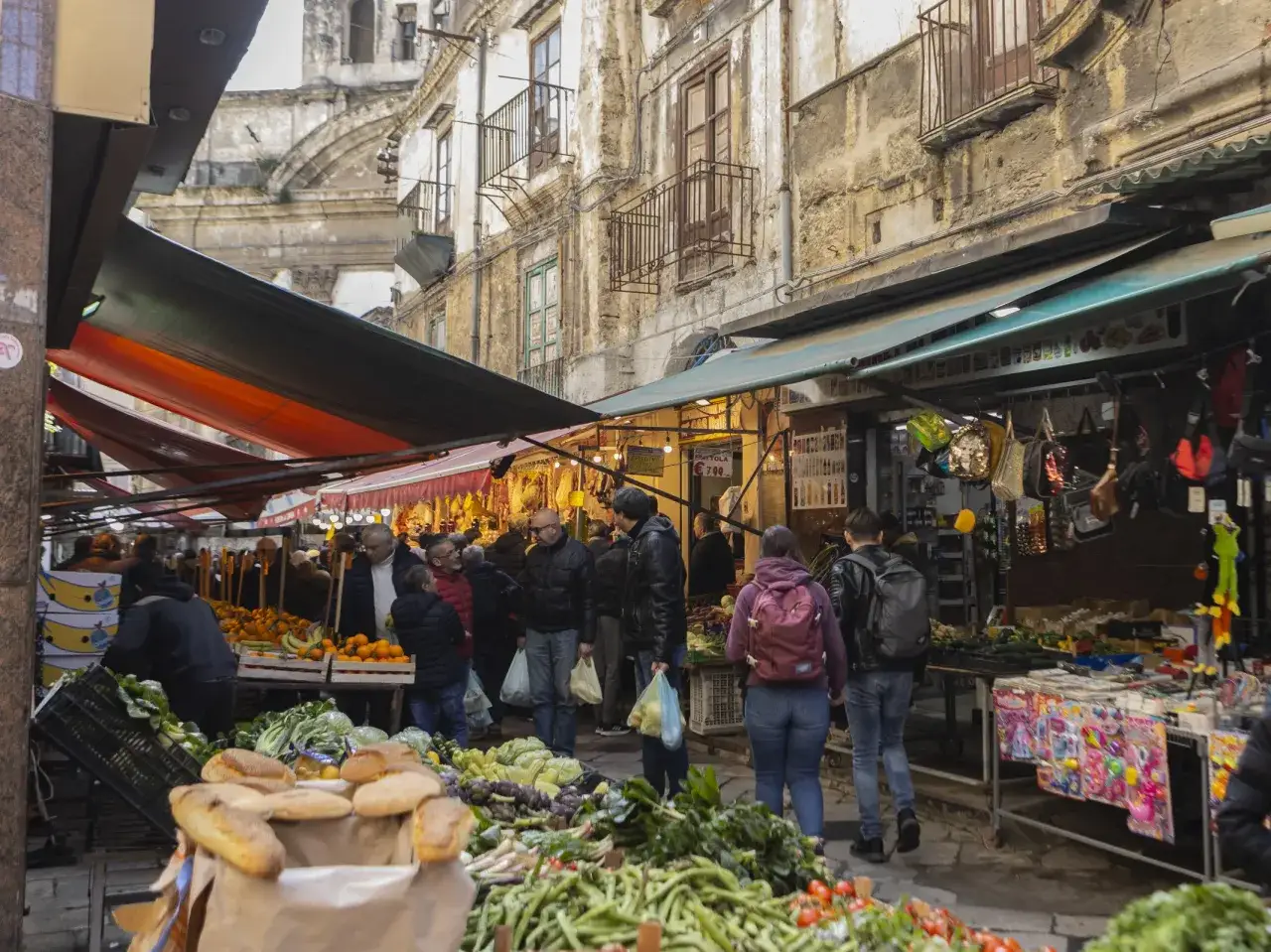 Ambiance anim&eacute;e d'un march&eacute; en plein air, id&eacute;al pour visiter Palerme. &Eacute;tals de fruits, l&eacute;gumes et pains frais sous des auvents color&eacute;s.