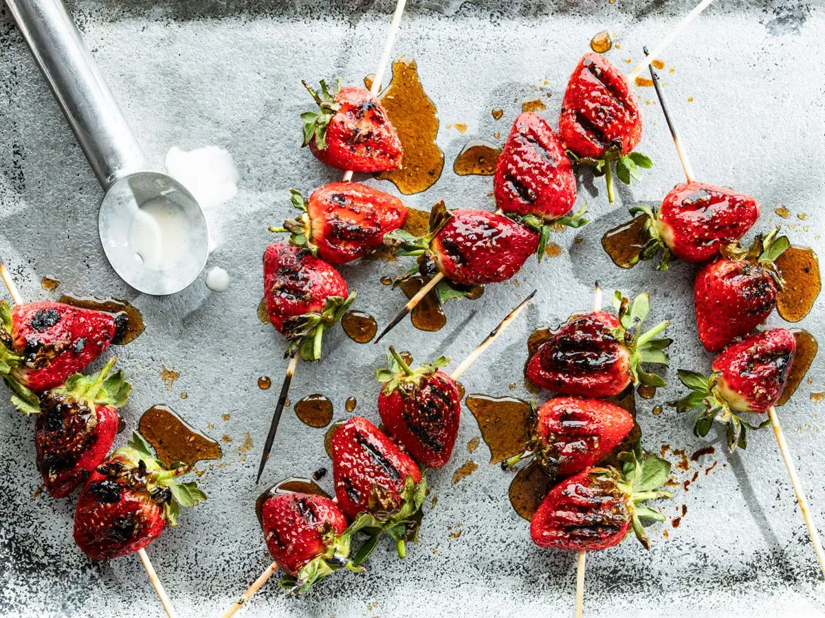 Erdbeeren grillen auf Spie&szlig;en, glasiert und mit Grillstreifen, auf einem Blech mit s&uuml;&szlig;er Sauce.