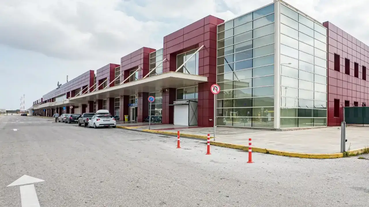 Modern byggnad vid Chania flygplats med röda fasader och stora glaspartier. Bilar står parkerade utanför.