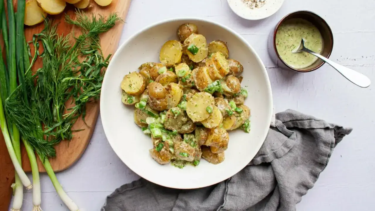 Salade de pommes de terre crémeuse, garnie d'herbes fraîches et d'oignons verts, servie avec une sauce salade onctueuse.