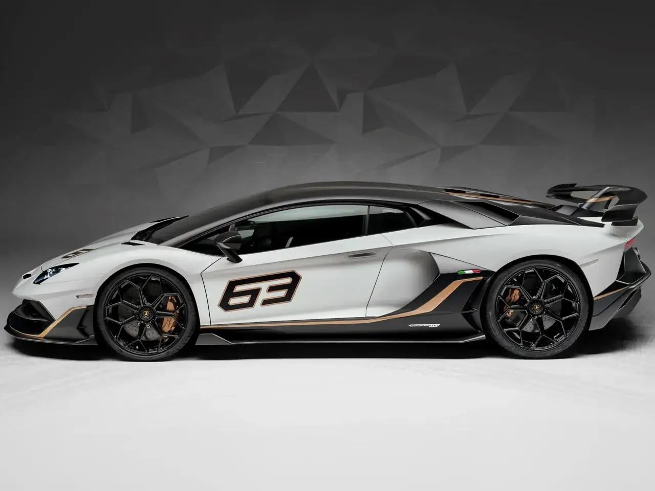 Biały Lamborghini Aventador z czarnymi akcentami i złotymi detalami, numer 63 na drzwiach.