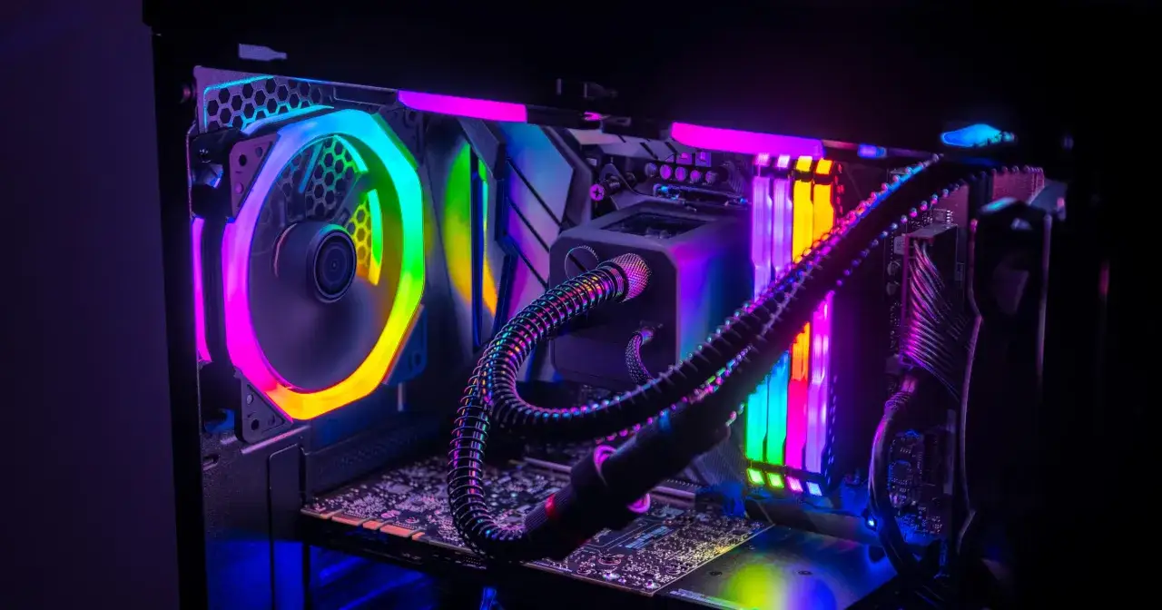 Wnętrze komputera z kolorowym podświetleniem RGB. Widoczne części komputera: wentylator, chłodzenie wodne, RAM, płyta główna.