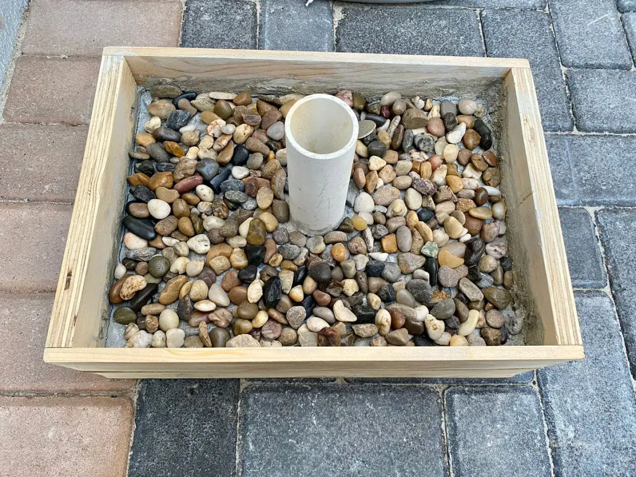 Base per ombrellone fai da te: un contenitore in legno riempito di ghiaia con un tubo centrale per l'asta.