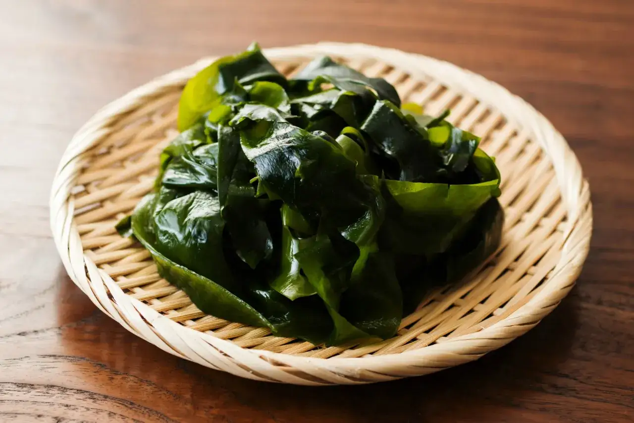 Zielone, błyszczące liście wodorostów wakame na plecionej tacce. Zastanawiasz się, wakame co to? To zdrowy składnik kuchni japońskiej.