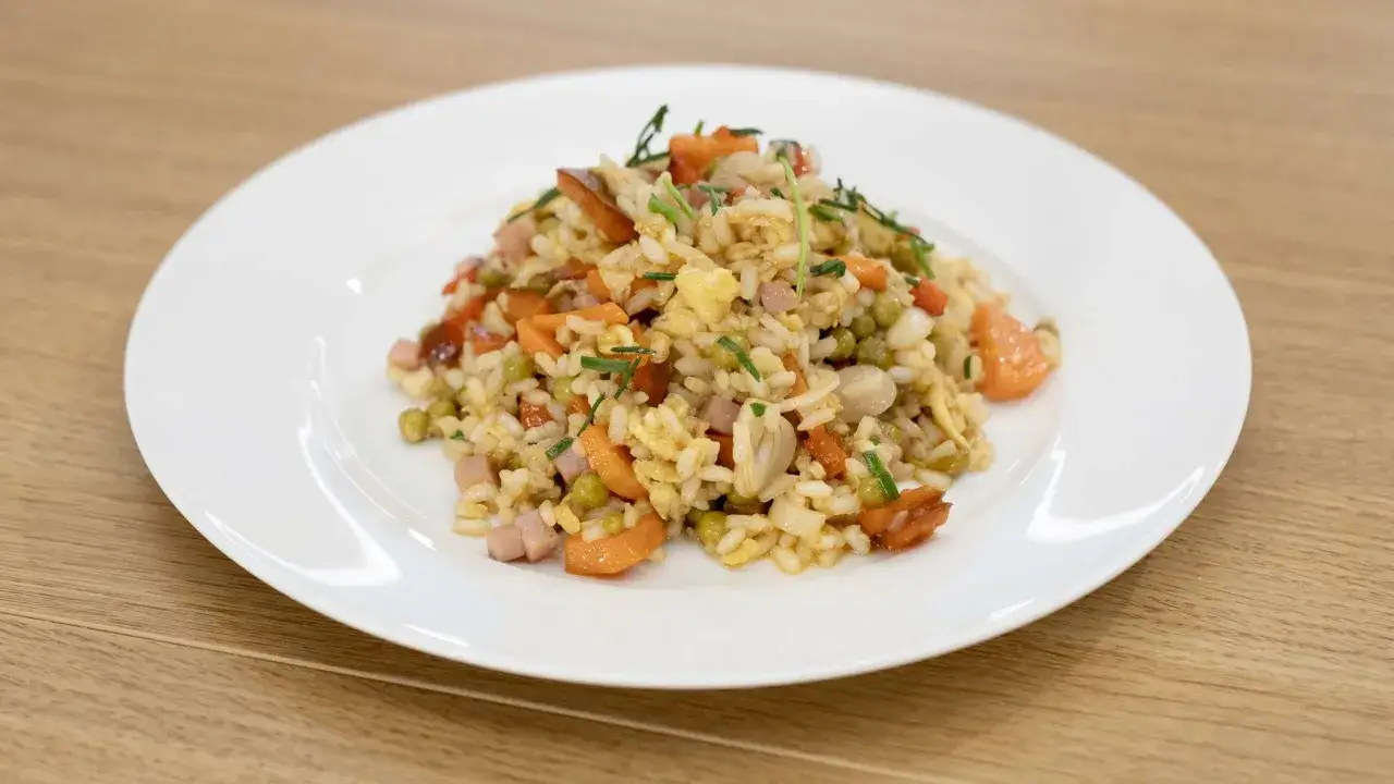 Un piatto di riso alla cantonese con piselli, carote, prosciutto e uovo strapazzato, guarnito con erba cipollina.